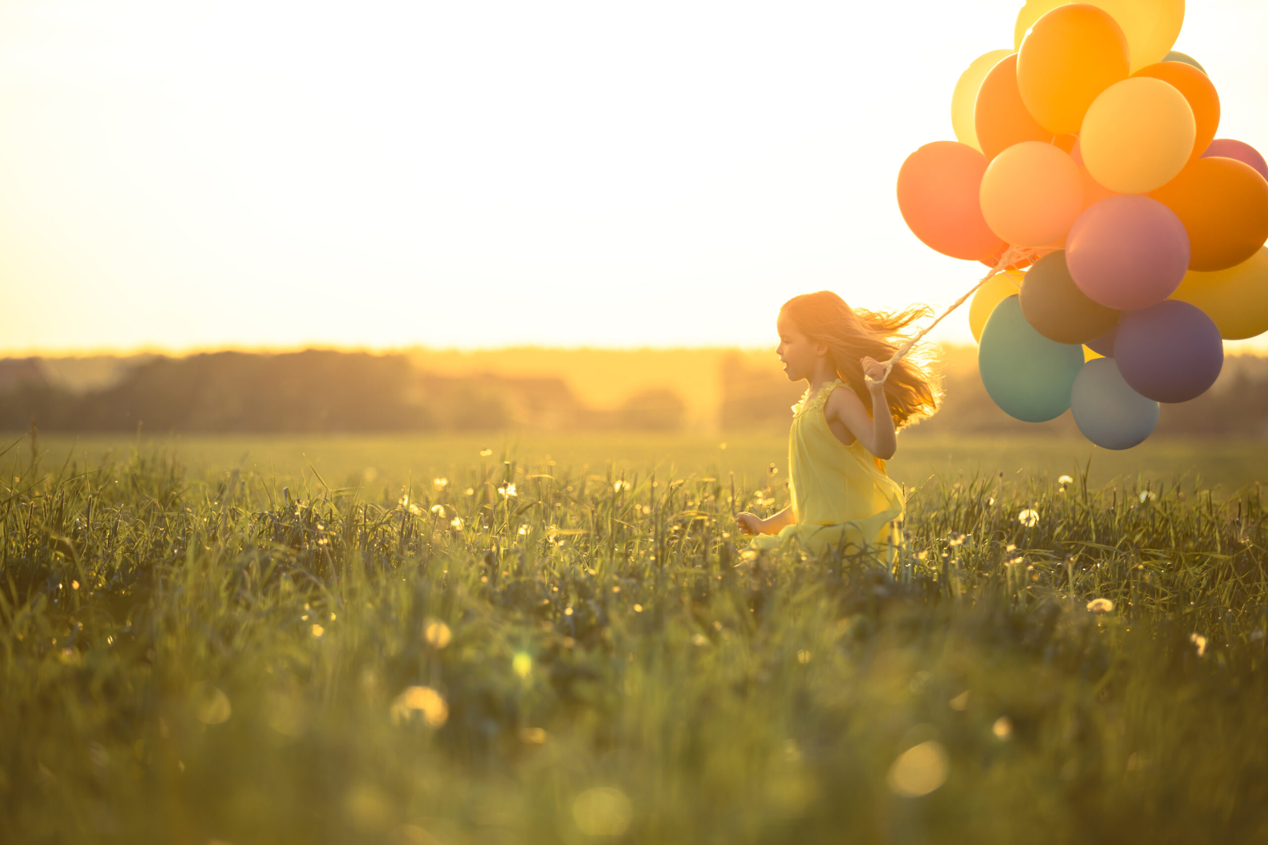 Little girl running through a field with balloons